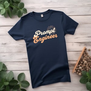 May include: A navy blue t-shirt with the text "Prompt Engineer" in a retro orange font with a firework graphic above the text.
