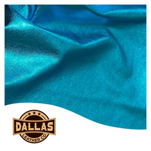 May include: Close-up of a vibrant, teal-coloured leather material with a metallic sheen. The fabric is folded, creating shadows and highlights that emphasise its texture. The Dallas Leather Co. logo is visible in the lower left corner.