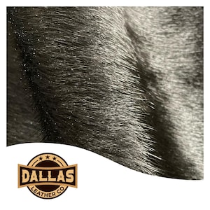 May include: Close-up of black leather with a textured surface. The leather has a slight sheen and visible grain. The Dallas Leather Co. logo is in the lower left corner, featuring a brown and gold design.
