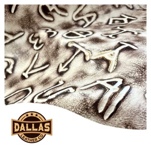 May include: Close-up of a piece of white leather with a brown, embossed pattern of letters and symbols. The leather has a textured surface. The image includes a logo for Dallas Leather Co.