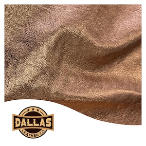 May include: Close-up of a textured, metallic rose gold leather. The leather has a wrinkled appearance with varying shades of gold and bronze. The Dallas Leather Co. logo is in the lower left corner.
