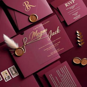 Puede incluir: Conjunto de invitaciones de boda burdeos con detalles dorados. Incluye invitación, tarjeta de confirmación y tarjetas de detalles, además de sobres sellados con sellos de cera. La invitación dice "Megan Jack" y "10 de septiembre de 2026".