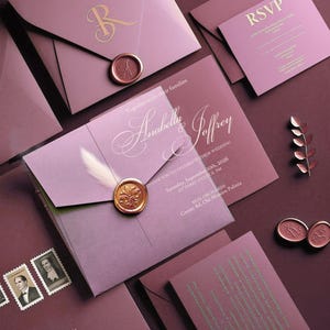 May include: A collection of mauve and burgundy wedding stationery, including invitations, RSVP cards, and details cards. Gold foil lettering and wax seals add a touch of luxury. The invitation reads "Anabella & Joffrey" and "Saturday, September 10th, 2026".