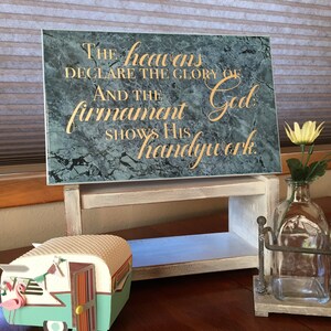May include: A wooden sign with a teal marble background and gold lettering. The sign reads "The heavens declare the glory of God. And the firmament shows His handywork."