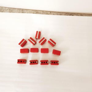 May include: A group of red electrical wire connectors with silver metal terminals. The connectors are arranged in a triangular shape with four rows.