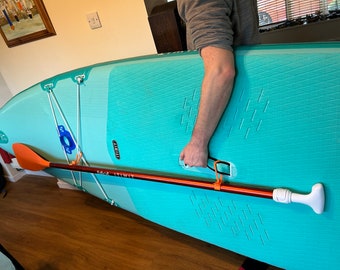 Op de afbeelding: Een turquoise opblaasbaar stand-up paddleboard met een oranje peddel en een witte handgreep. Het paddleboard heeft een getextureerd oppervlak en een witte band.