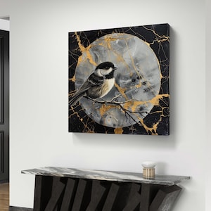 Könnte beinhalten: Ein abstraktes Gemälde in Schwarz und Gold mit einem weißen Kreis in der Mitte. Der Kreis zeigt einen kleinen schwarz-weißen Vogel, der auf einem Ast sitzt. Das Gemälde ist gerahmt und hängt an einer weißen Wand.