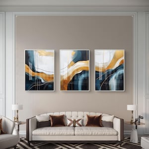 Puede incluir: Tres obras de arte abstractas enmarcadas. Cada pieza presenta una mezcla de azul marino, dorado y blanco con líneas y formas fluidas. La obra de arte se exhibe sobre un sofá con cojines marrones, creando una estética de sala de estar moderna.