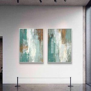 May include: Two framed abstract paintings with teal, brown, and white vertical brushstrokes. The artwork is displayed on a white wall in a gallery setting. The paintings have a reflective surface and are mounted in silver frames.