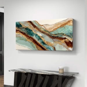Puede incluir: Arte abstracto en lienzo con un diseño fluido con acentos turquesa, marrón y dorado. La obra de arte está colgada en una pared blanca sobre una consola moderna negra y gris. La paleta de colores incluye tonos turquesa, marrón, dorado y blanco.