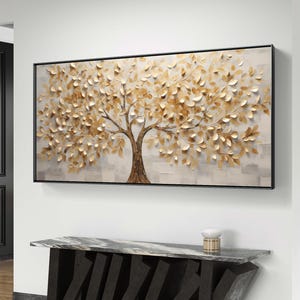 May include: A gold leaf tree painting with a textured, 3D effect. The painting is framed in black and hangs on a white wall above a black marble table.