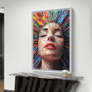 以下が含まれることがあります： カラフルな筆で構成された女性の顔を描いた額入りのアートワーク。顔は目を閉じ、赤い唇をしています。筆は外側に放射状に広がり、鮮やかで芸術的な肖像画を作り出しています。アートワークは、黒とグレーのコンソールテーブルの上に展示されています。
