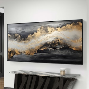 Op de afbeelding: Abstract schilderij met zwarte, witte en gouden verf. Het schilderij is ingelijst in een zwart frame en hangt aan een witte muur boven een zwarte en marmeren consoletafel.