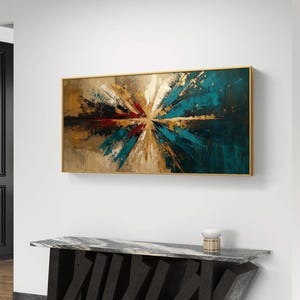 Puede incluir: Pintura de arte abstracto en un marco dorado. La obra presenta una explosión de colores, incluyendo turquesa, dorado, marrón y rojo, que irradian desde el centro. La pintura está montada en una pared blanca sobre una consola de mármol negro y gris.