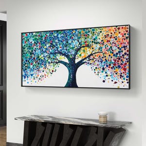 Puede incluir: Pintura abstracta enmarcada de un árbol con tronco y ramas oscuras. Las hojas del árbol están representadas por puntos de colores en tonos azules, verdes, amarillos, naranjas y rojos. La obra de arte se exhibe sobre una consola moderna.