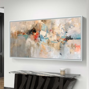 May include: Abstract painting in shades of beige, brown, blue, and pink. The painting is framed in a white frame and is hanging on a white wall above a black marble console table.