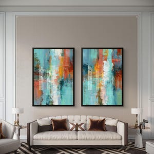 May include: Two framed abstract art pieces with a black border. The artwork features vertical brushstrokes in shades of teal, orange, white, and navy blue. The paintings are displayed above a white sofa with brown throw pillows.