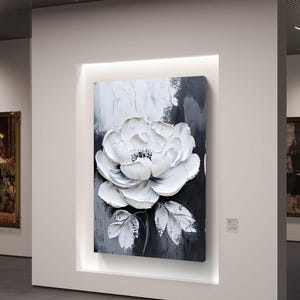 Puede incluir: Pintura de una gran flor de peonía blanca texturizada sobre un fondo negro y gris. La obra de arte se exhibe en un marco blanco empotrado, creando una presentación tipo galería. Los pétalos son gruesos y detallados.