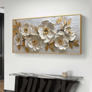 May include: A large, rectangular canvas painting with a gold frame. The painting features a white floral design with gold accents. The flowers are in a 3D style, giving the painting a textured look.