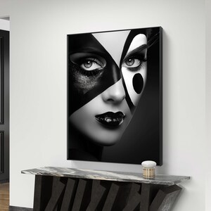 Close-up black and white portrait of a woman with bold, artistic face paint featuring geometric shapes and high contrast. Her lips are painted black, and her eyes are highlighted with striking eye makeup.
