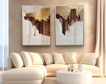 May include: Two framed abstract art pieces with gold, brown, and white textured designs. The artwork features gold accents and a dripping effect. The frames are gold, and the art hangs above a cream-colored sofa.
