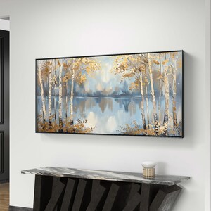 May include: A framed painting of a lake scene with trees in the foreground and a reflection of the trees in the water. The trees are painted in shades of gold and white, and the water is painted in shades of blue and gray.