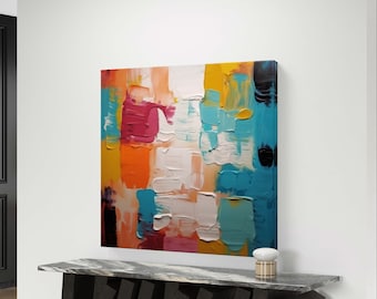 May include: Abstract painting with bold strokes of orange, yellow, pink, blue, and white paint. The painting is hanging on a white wall above a black marble console table with a geometric design.