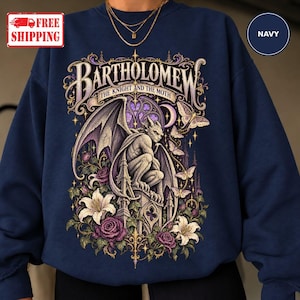 May include: A navy blue crewneck sweatshirt featuring a graphic print of a gargoyle perched on a stone structure. The text reads BARTHOLOMEW THE KNIGHT AND THE MOTH. The design includes purple roses, white lilies, moths, a crescent moon, and gothic architectural elements.