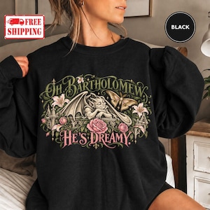 May include: A black crewneck sweatshirt featuring a graphic print of a gargoyle resting on a stone ledge, surrounded by pink roses, white lilies, and a moth. The text reads, "Oh Bartholomew, He's Dreamy" in a decorative, stylized font.