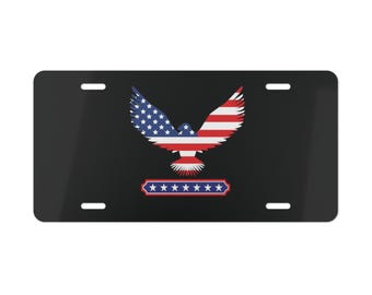 May include: Black license plate featuring a stylized eagle with outstretched wings. The eagle design incorporates the American flag's stars and stripes in red, white, and blue. A banner with stars is below the eagle.
