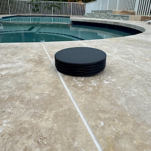 Könnte beinhalten: Ein Stapel schwarzer Pool-Schwimmhilfen auf einer beige gefliesten Oberfläche in der Nähe eines Schwimmbeckens.