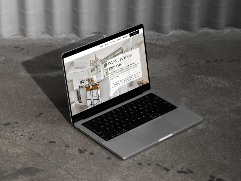 May include: A laptop computer displaying a website with the text "Invest in your dreams". The website features a photo of a modern kitchen with white cabinets, a stainless steel refrigerator, and a large chandelier.