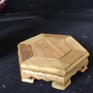 May include: A wooden hexagonal display stand with a light brown finish. The stand has a multi-faceted top and decorative curved edges. The stand is approximately 4 inches wide and 3 inches tall.