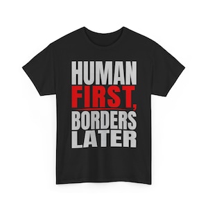 Può includere: T-shirt nera con la scritta "HUMAN FIRST, BORDERS LATER" in lettere bianche e rosse. La maglietta, a girocollo, sembra essere realizzata in cotone o tessuto simile. Il testo è centrato sulla parte anteriore del capo.