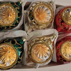 Puede incluir: Seis adornos navideños vintage en una caja. Los adornos tienen forma de lágrima con un borde dorado y un diseño dorado. Dos son verdes, dos son blancos y dos son rojos.
