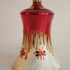 May include: A red and white glass Christmas ornament shaped like a bell with gold glitter accents and red glitter stars.