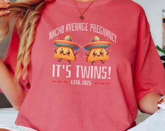 May include: A pink t-shirt with the text "Nacho Average Pregnancy It's Twins! Est. 2025" and a cartoon image of two smiling nacho chips wearing sombreros.