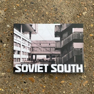 May include: A monochrome photograph of Soviet architecture. The image shows a stark contrast between light and shadow, with the text "SOVIET SOUTH" in bold white letters at the bottom. The buildings are concrete and angular.
