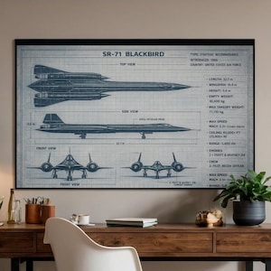 Puede incluir: Un escritorio de madera con patas de metal negro, una silla blanca y un plano enmarcado de un avión SR-71 Blackbird. El plano está en tonos azules y blancos, con dibujos técnicos y especificaciones. Una lámpara colgante negra cuelga sobre el escritorio.