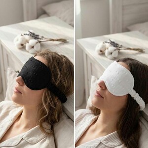 May include: Two eye masks, one black and one white, are shown in this image. Both masks have a textured, dotted pattern and a strap to secure them. The black mask is on the left, and the white mask is on the right. The masks are designed for sleep and relaxation.