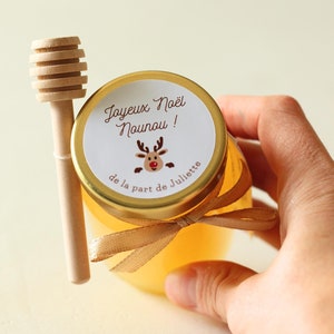 Peut inclure: Petit pot de miel avec un couvercle doré et un dipper en bois. Le couvercle porte une étiquette avec une illustration de renne et le texte "Joyeux Noël Nounou!". Un ruban est noué autour du pot.