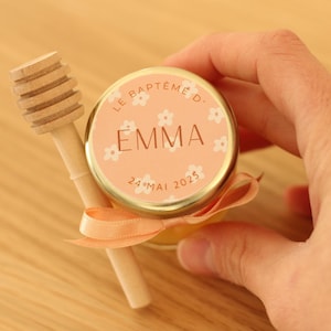 Peut inclure: Un petit pot de miel en verre avec une étiquette de couleur pêche qui dit "Le Baptême d'Emma 24 Mai 2023". Le pot est attaché avec un ruban de couleur pêche et est livré avec un bâtonnet à miel en bois.