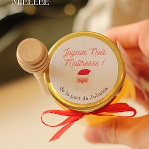 Petit pot de miel personnalisé avec étiquette 'Joyeux Noël Maîtresse', illustration de Père Noël, ruban rouge et cuillère en bois. Cadeau artisanal et local idéal pour remercier les enseignants à Noël, produit dans la Drôme par La Belle Miellée