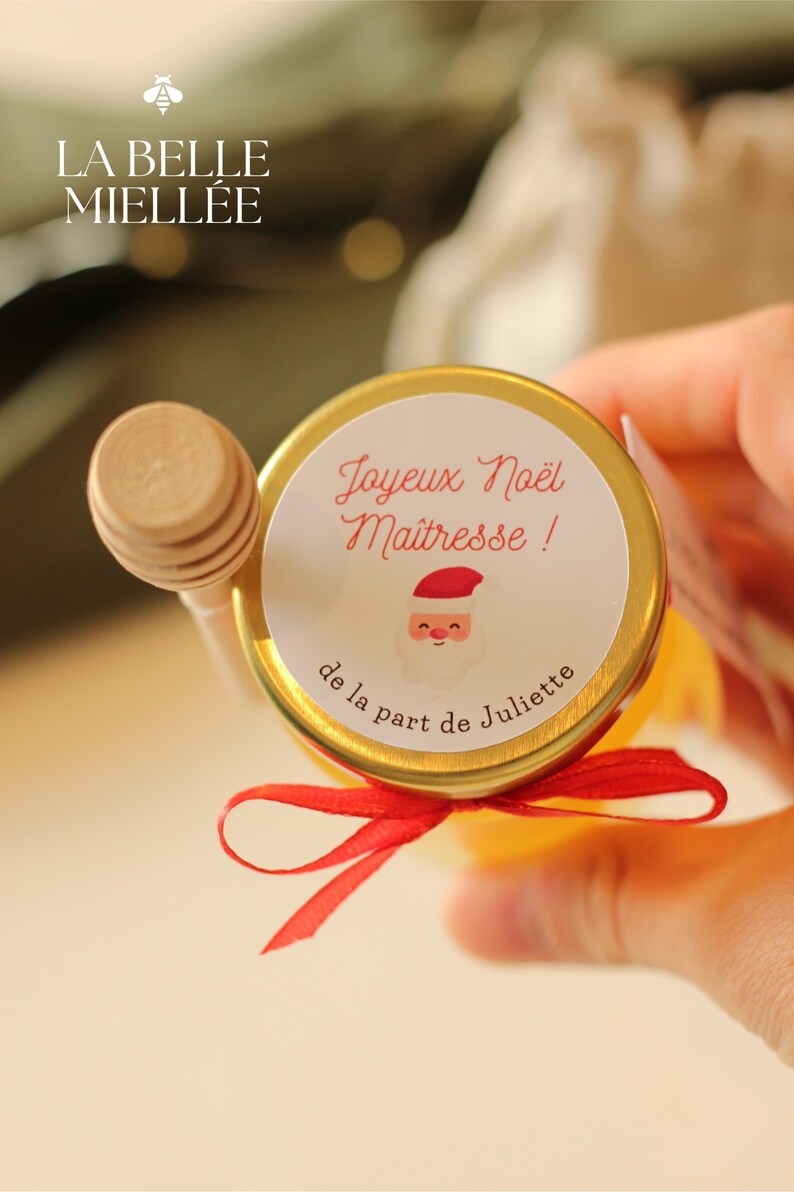 Petit pot de miel personnalisé avec étiquette 'Joyeux Noël Maîtresse', illustration de Père Noël, ruban rouge et cuillère en bois. Cadeau artisanal et local idéal pour remercier les enseignants à Noël, produit dans la Drôme par La Belle Miellée