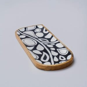May include: A rectangular wooden tray with a black and white geometric pattern. The tray has rounded edges and a natural wood finish.