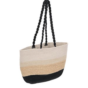 Puede incluir: Un bolso tote tejido con una combinación de colores crema, beige y negro. El bolso tiene un asa de cuerda negra trenzada. El diseño incluye una parte superior crema, una sección media beige y una base negra.