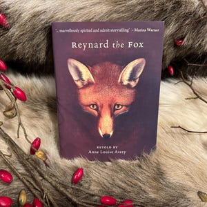 Può includere: Un libro intitolato "Reynard the Fox"  rivisitato da Anne Louise Avery. La copertina presenta un primo piano del muso di una volpe su uno sfondo marrone scuro.