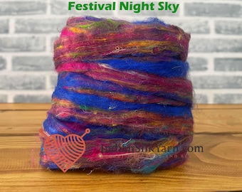 May include: A vibrant bundle of yarn in shades of blue, pink, purple, and yellow. The yarn is tightly wound, creating a textured appearance. The text "Festival Night Sky" is at the top. A heart-shaped logo with a yarn design is on the bottom left.