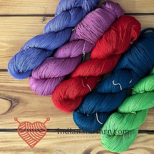 May include: Five skeins of twisted yarn in vibrant colors including blue, purple, red, dark blue, and green. A logo featuring a heart shape made of yarn with the text Indiansilkyarn.com and the words LUXURY ELEGANCE is visible in the corner.