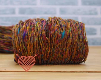 May include: A close-up of a vibrant, multi-colored yarn ball. The yarn features a blend of orange, yellow, red, blue, and purple hues. The yarn is tightly wound, showcasing its texture and color variations. The image is of a craft supply, perfect for knitting or crochet projects.